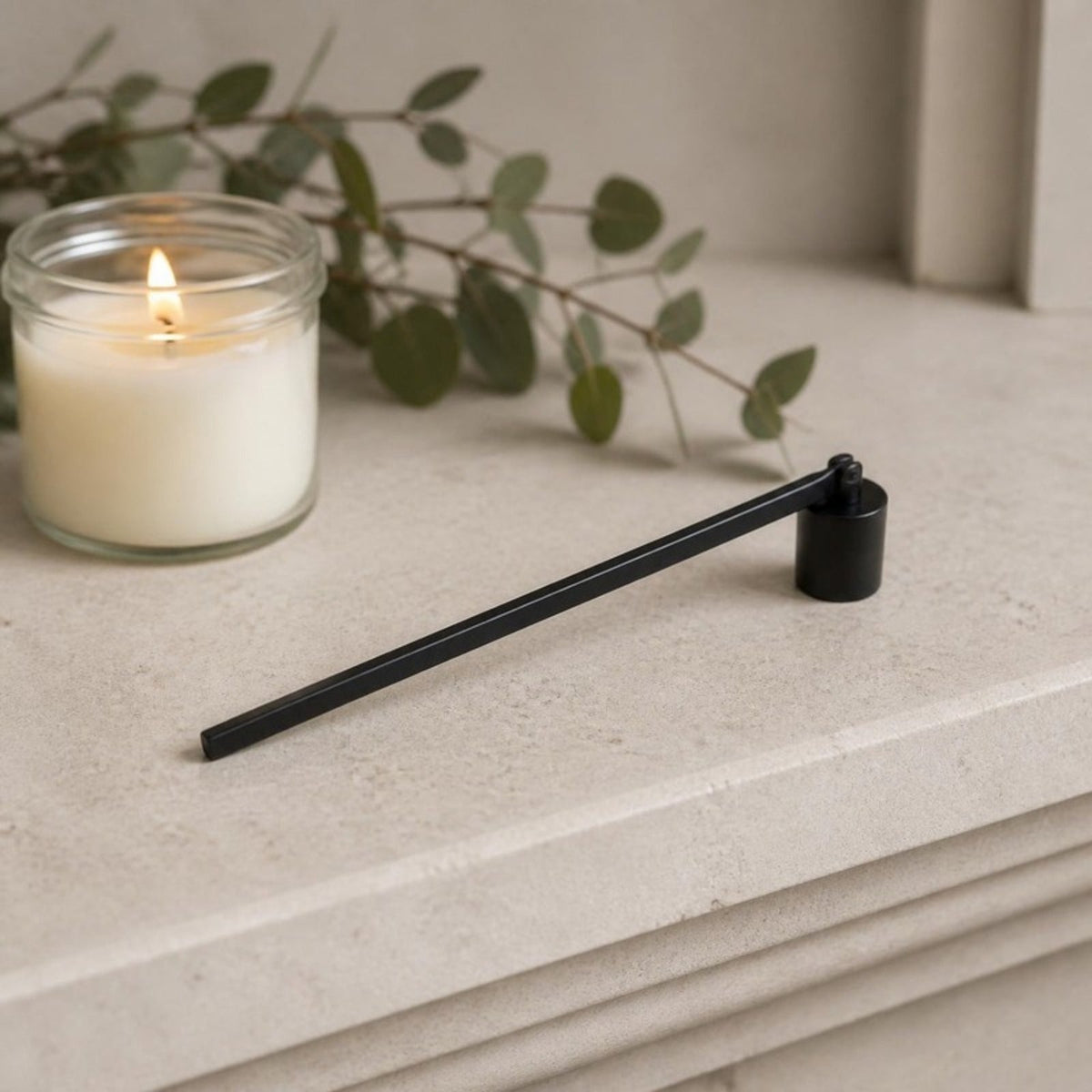 Black candle snuffer on a mantel beside a lit candle